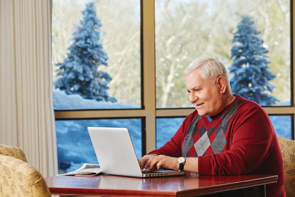 winter sadness Man sits at a table with a laptop. He is indoors but there is snow outside.