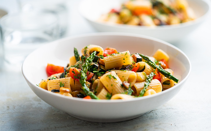 Close-up shot of a delicious looking white bowl full of pasta and vegetables.