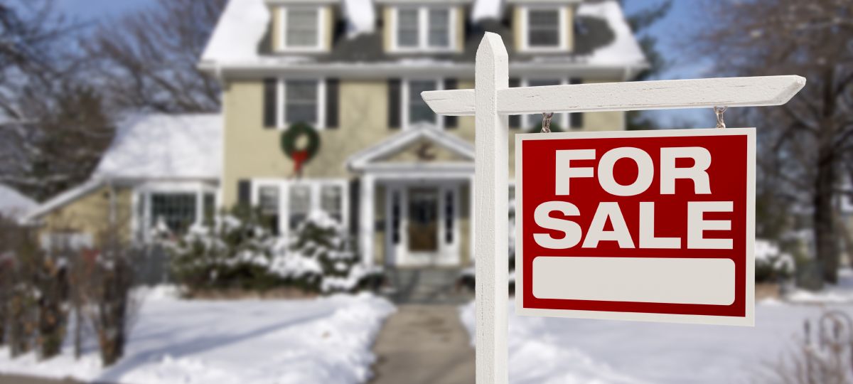 Sell your house this winter A house covered in snow with a "for sale" sign in front.
