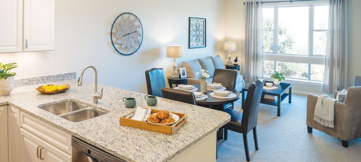Interior shot of kitchen facing a bright, furnished spacious living room.