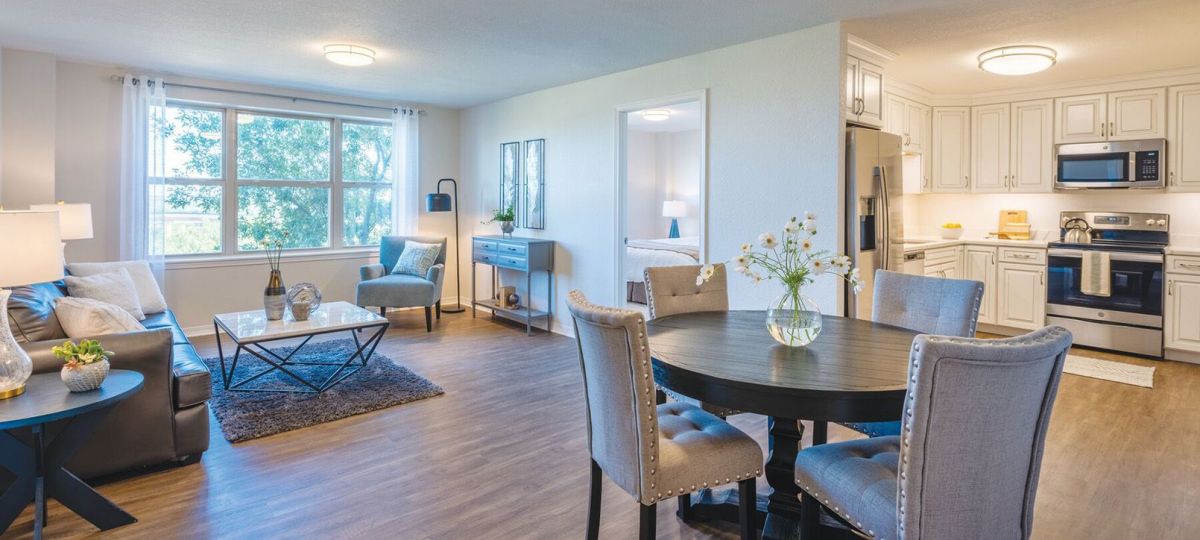 Wide shot of a bright and open living room, kitchen, and dining room in a two-bedroom apartment.