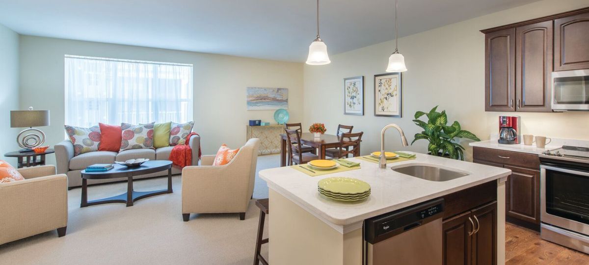 Wide shot of a bright and open living room, kitchen, and dining room in an Erickson apartment.