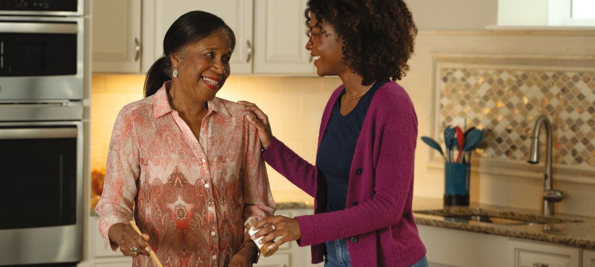 A resident and her adult daughter laugh together as they cook in an Erickson apartment kitchen. 