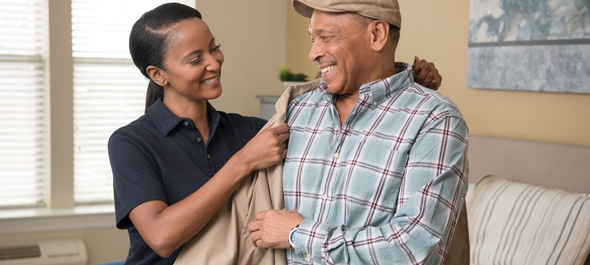 A cheery Erickson employee assists a smiling resident with putting on his coat. 