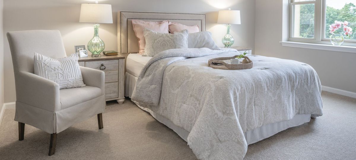 A cozy senior apartment bedroom with soft lighting, plush armchair.