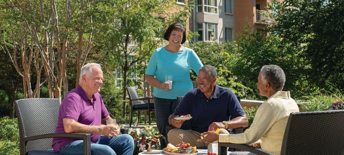 A diverse group of residents gather outside talking and laughing in an Erickson community courtyard.
