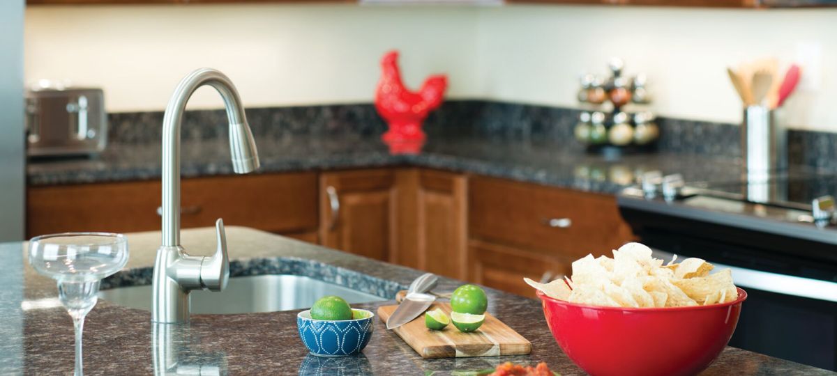 Close-up shot of a modern kitchen counter with a large red bowl full of delicious looking tortilla chips, a cutting board with sliced limes and a small bowl of red salsa.