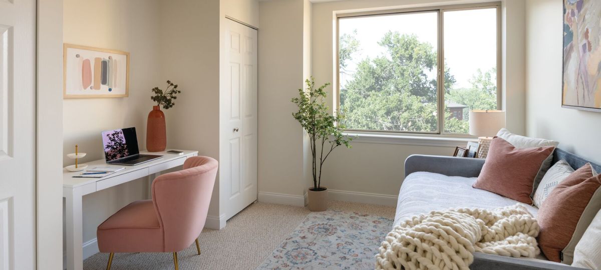 Cozy den with plush armchair, desk and chair, and large window letting in natural light - designed for comfort and relaxation in an Erickson apartment.