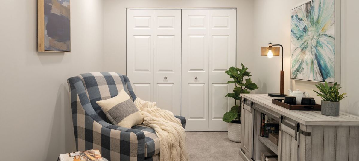 Cozy den with plush armchair and footstool, television sitting on top of an entertainment unit, and large double doors - designed for comfort and relaxation in an Erickson apartment.