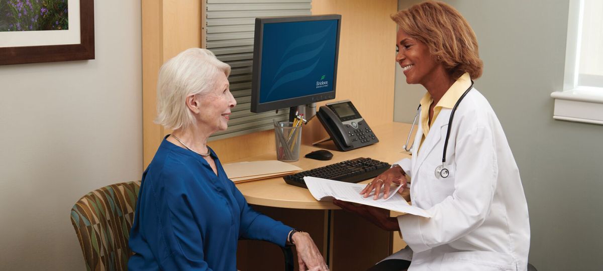 An African American female doctor is smiling and talking with a patient at an Erickson onsite medical center. 