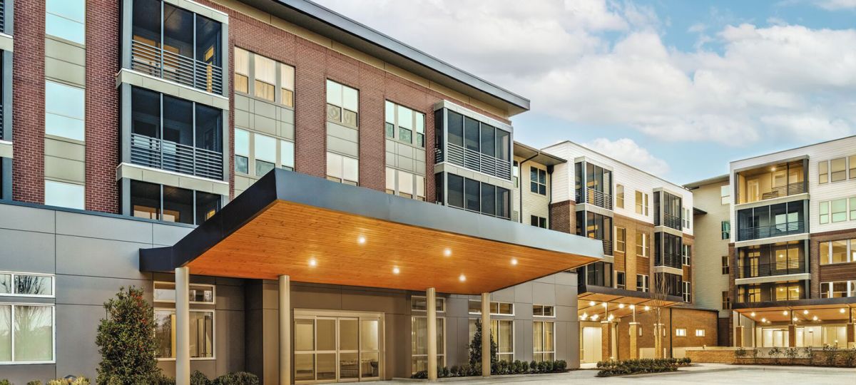 Exterior view of a Woodleigh Chase residential building, part of Erickson Senior Living, featuring modern architecture surrounded by modern lighting, hardscaping and a clear blue sky.