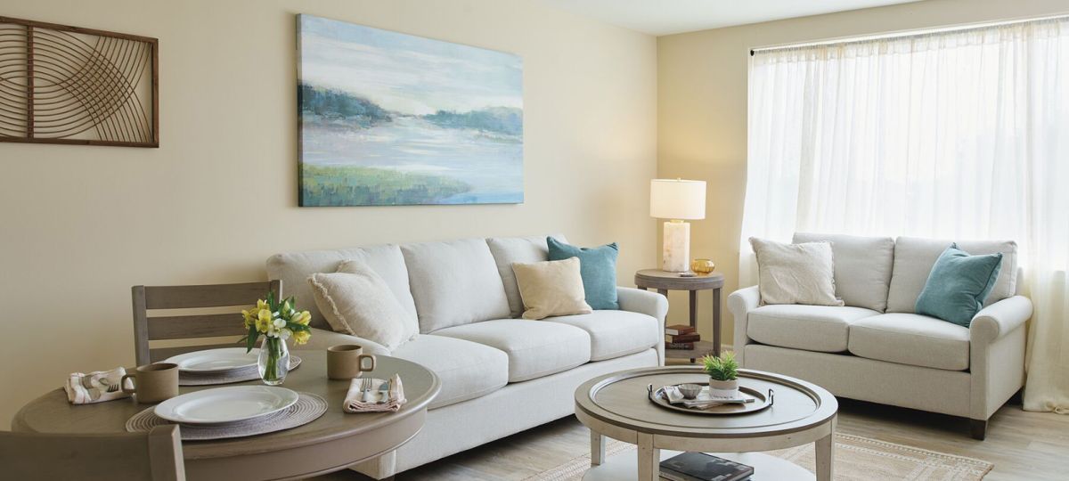 Comfortable and well-furnished living room with comfortable, white couch and sofa, with a large balcony window.