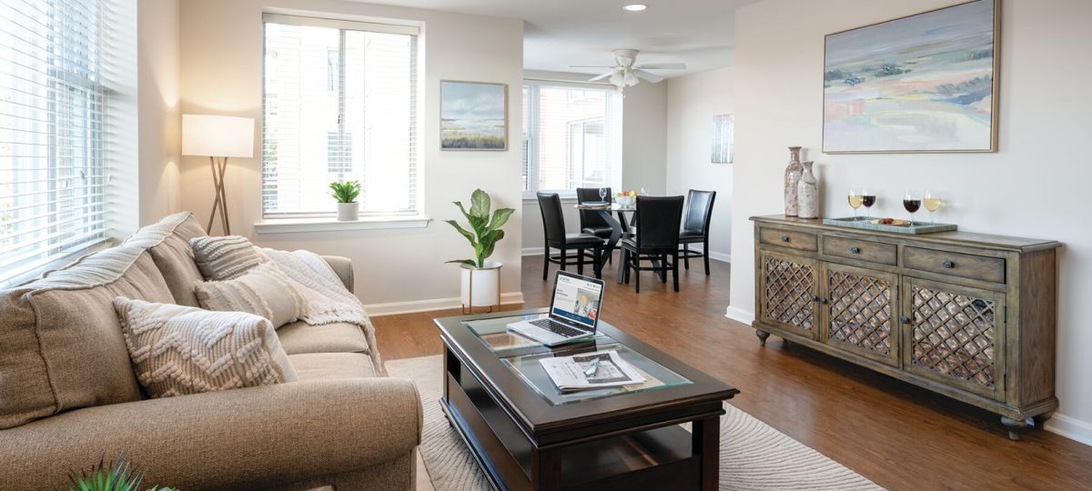 Bright and modern living room with neutral tones, featuring a beige sofa, wooden coffee table, accent chairs, and a large window.