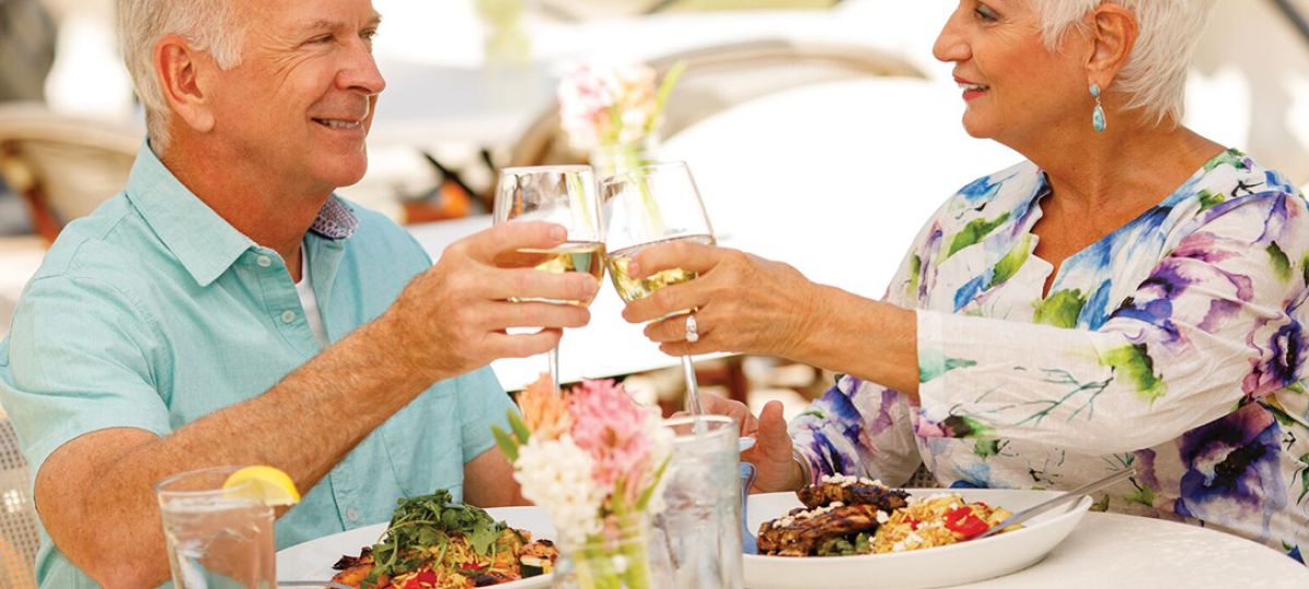 Couple enjoys outdoor dining at Siena Lakes, an Erickson Senior Living community, toasting wine glasses in a relaxed setting.