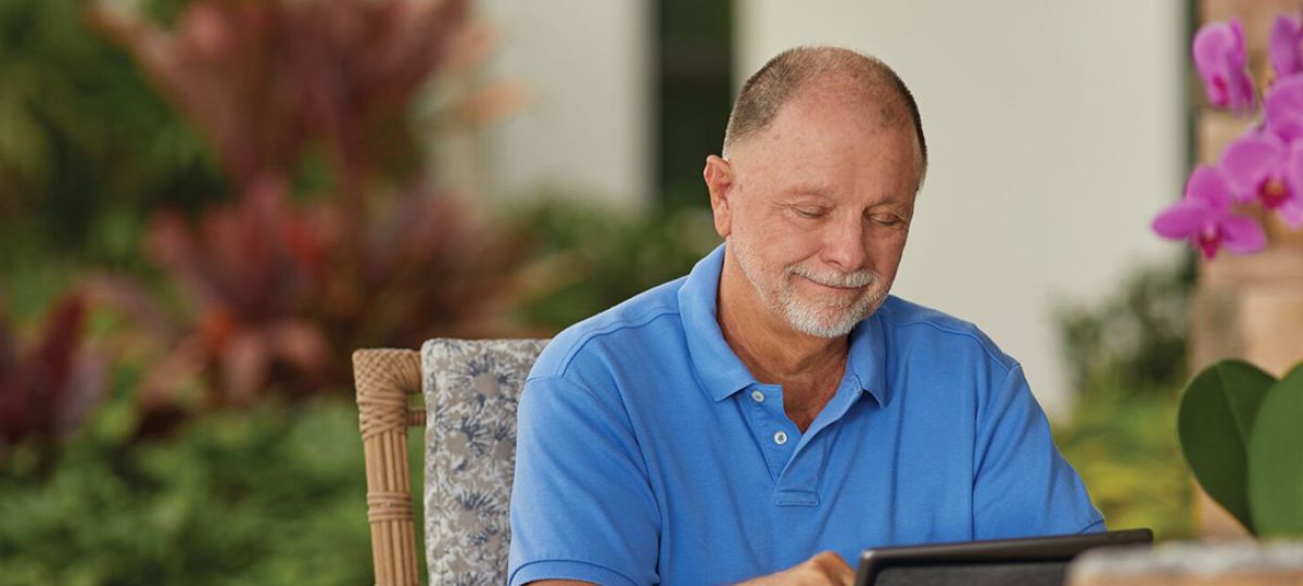 Man relaxing outside his apartment, working on a laptop in a sunny courtyard.