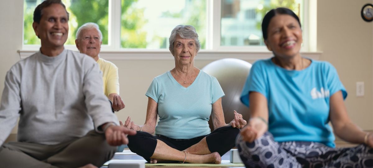 Two men and two women are in a yoga studio doing yoga. They are currently cross-legged on the floor.