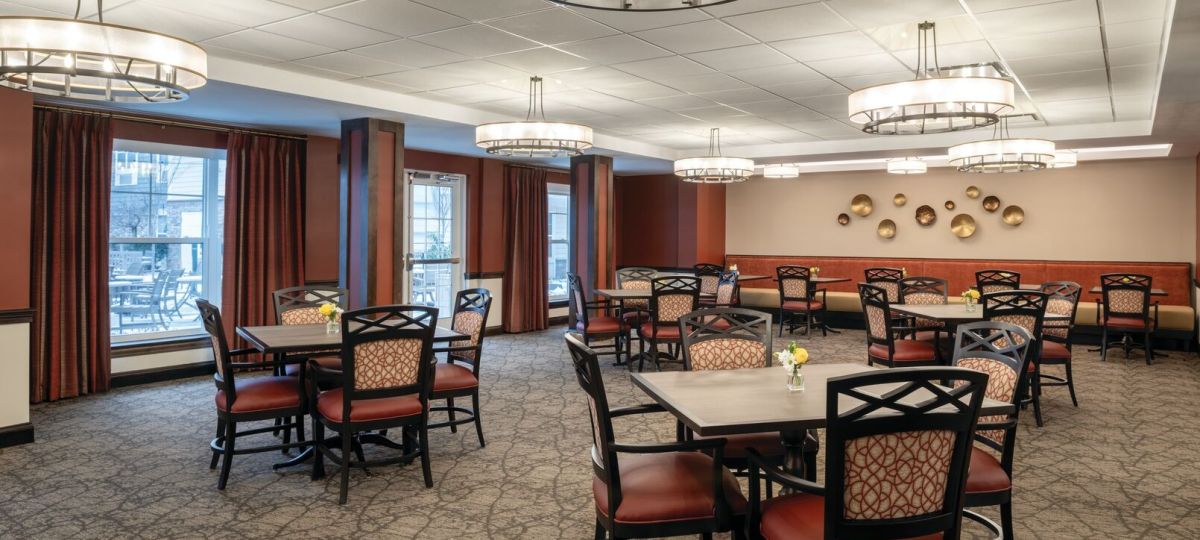 Spacious dining room with multiple tables, patterned chairs, large modern light fixtures, and decorative wall accents.