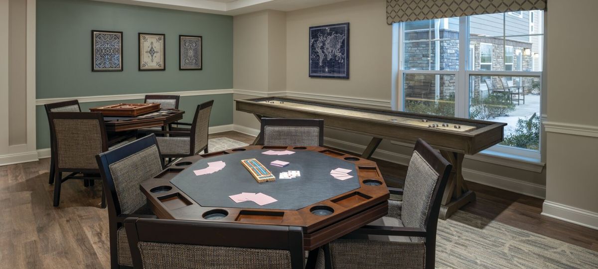 Game room with a poker table set with cards, additional seating, and a long shuffleboard table near a large window.
