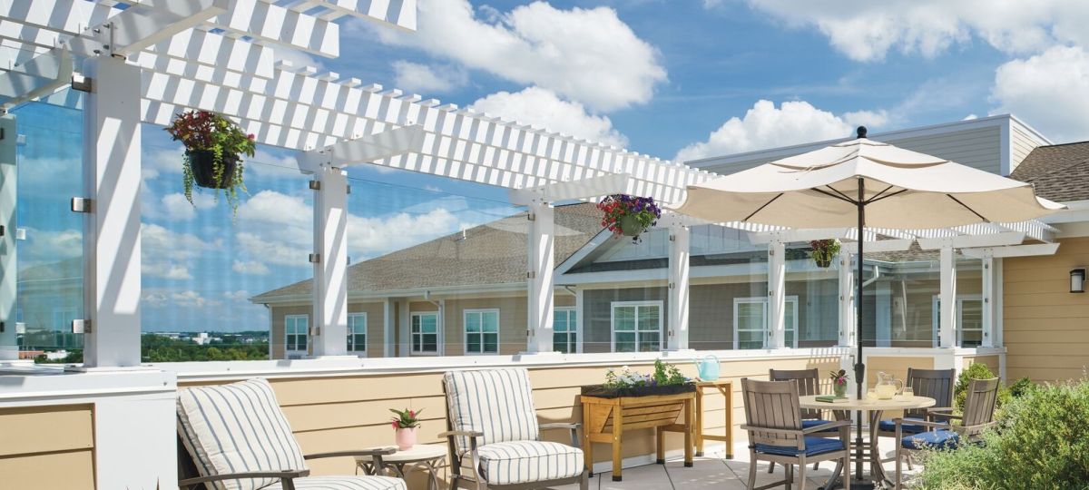 Outdoor rooftop patio with lounge chairs, umbrella‑shaded seating, hanging plants, and pergola-style overhead beams.