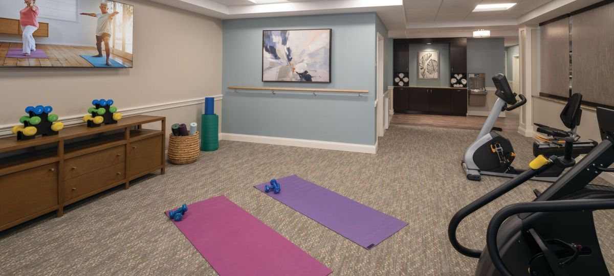 Fitness and wellness room with exercise mats, dumbbells, stationary bikes, and a balance barre along the wall.