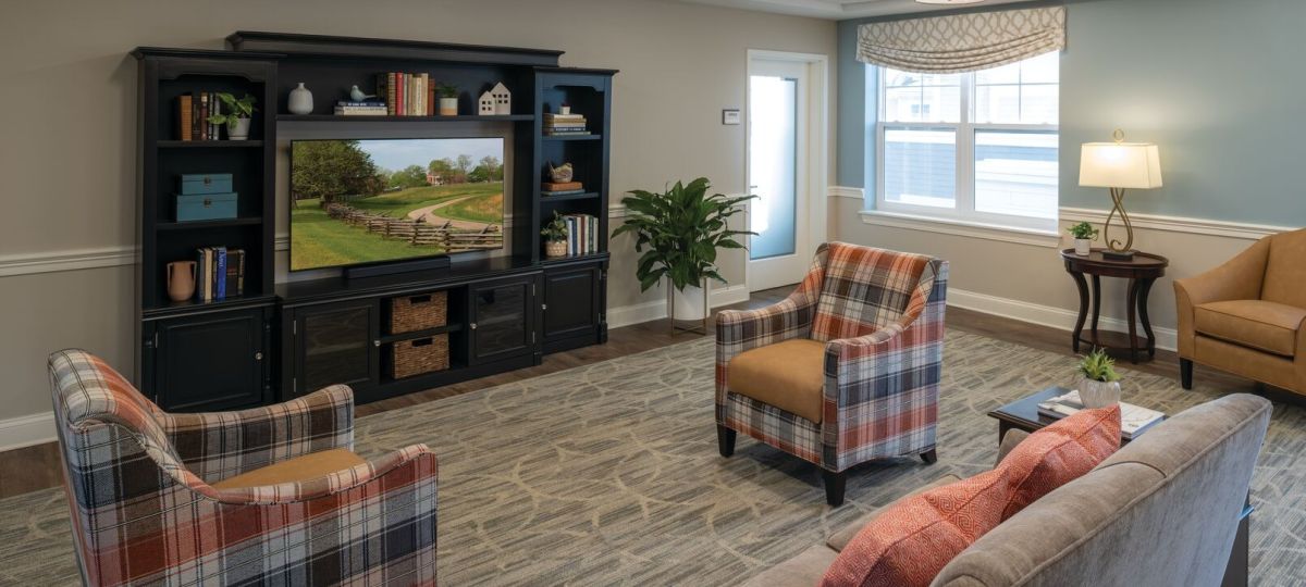Comfortable lounge area with plaid armchairs, sofa seating, a large media cabinet, and windows providing natural light.