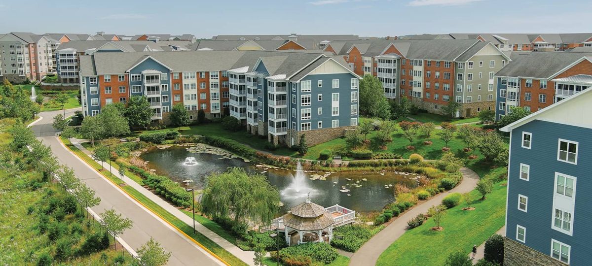 Aerial exterior shot of Ashby Ponds community buildings with surrounding greenery, pond, and a beautiful blue sky.