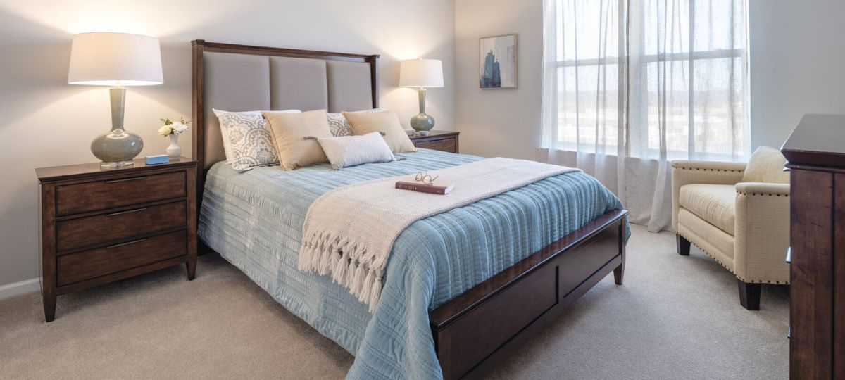 Spacious bedroom with upholstered bed, wooden furniture, bedside lamps, and large window with natural light.