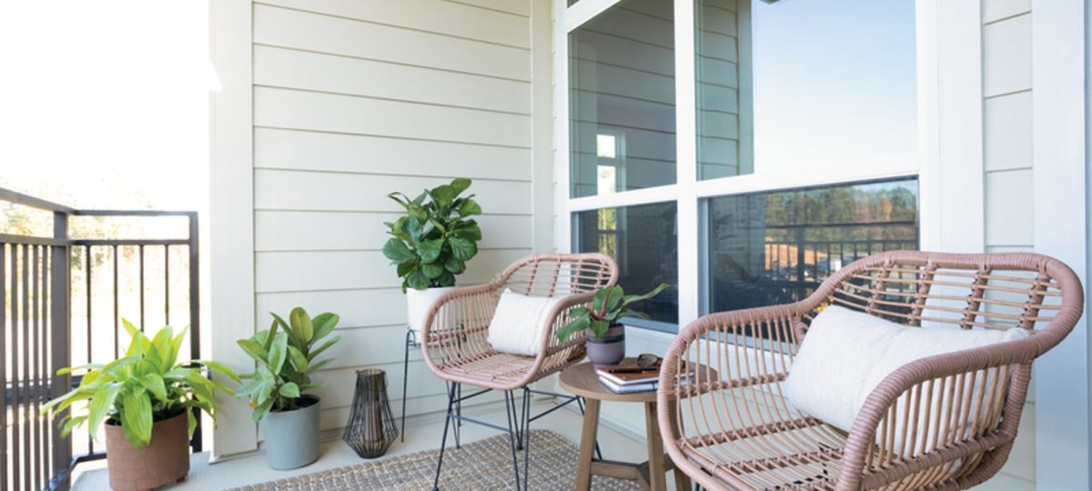 Cozy outdoor balcony with two wicker chairs, a small table, and potted plants, creating a relaxing seating area with natural light.