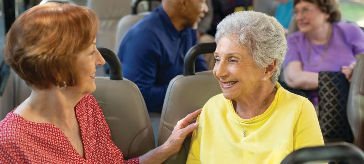 Older adults chatting and smiling while riding together in a community shuttle bus.