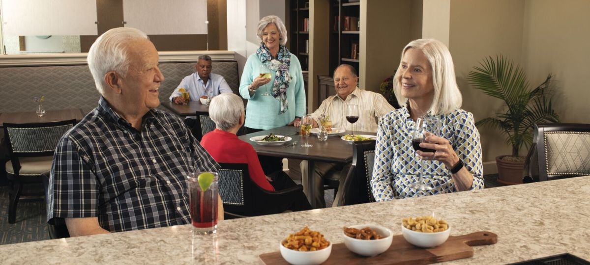 Group of older adults socializing at a bar area, enjoying drinks and conversation in a community setting.
