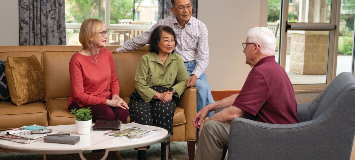Group of older adults sitting together in a cozy living room, engaged in friendly conversation around a coffee table.
