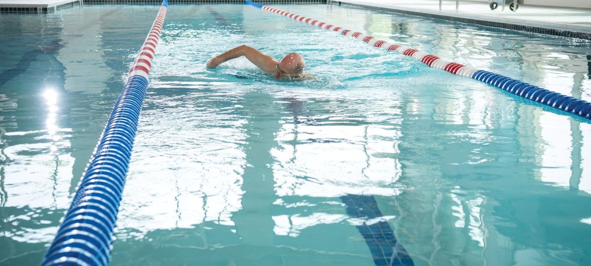 Older adult swimming laps in an indoor pool with lane dividers in a senior living fitness facility.