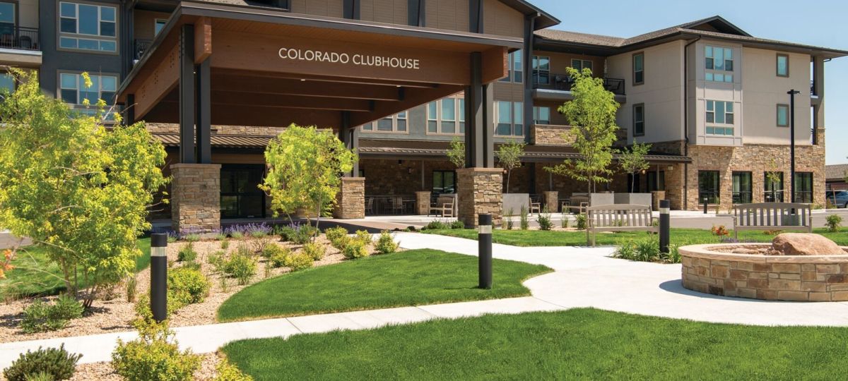 Modern Erickson Senior Living clubhouse building with landscaped lawn, walking paths, and outdoor seating.