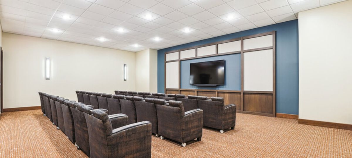 Modern community theater room with rows of comfortable chairs facing a large screen.