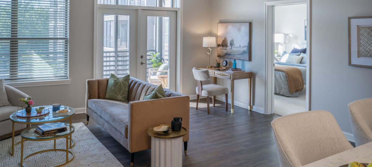Bright living room with modern sofa, glass coffee table, large windows, and balcony access with natural light.