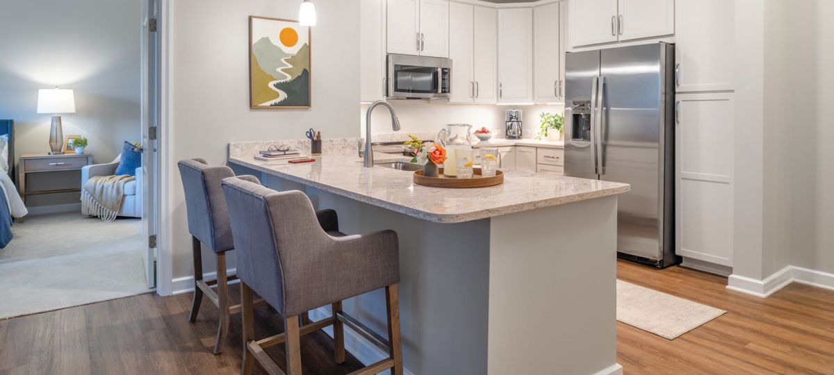 Bright modern kitchen with white cabinets, granite island with bar stools, stainless steel appliances, and open layout.