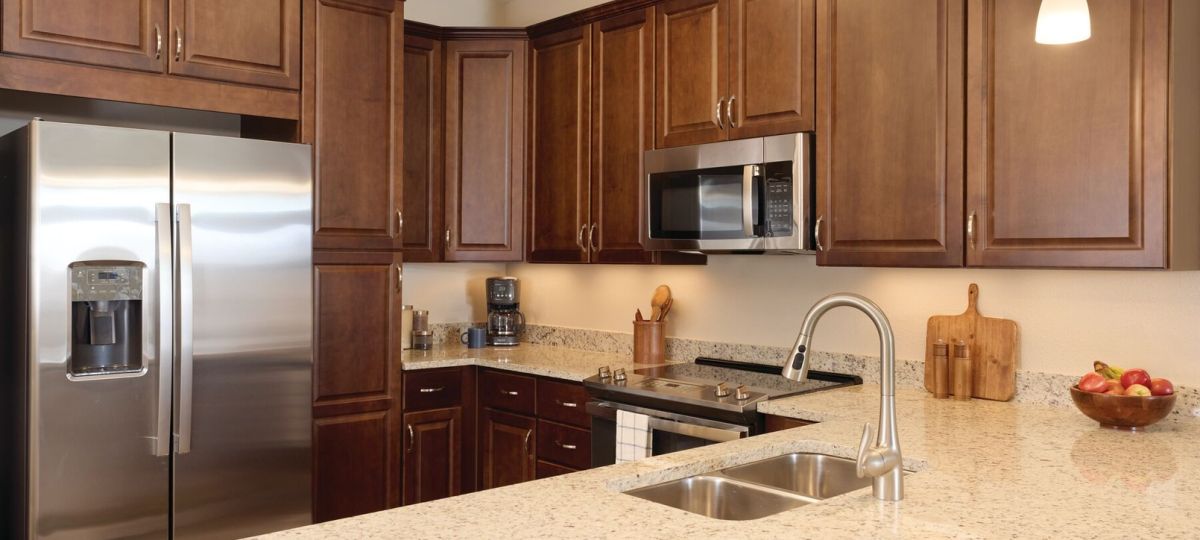 Modern apartment kitchen with dark wood cabinetry, granite countertops, stainless steel appliances, and pendant lighting.