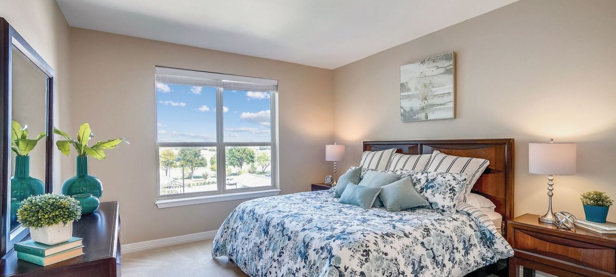 Bright bedroom with floral bedding, large window, wood furniture, and soft neutral decor.