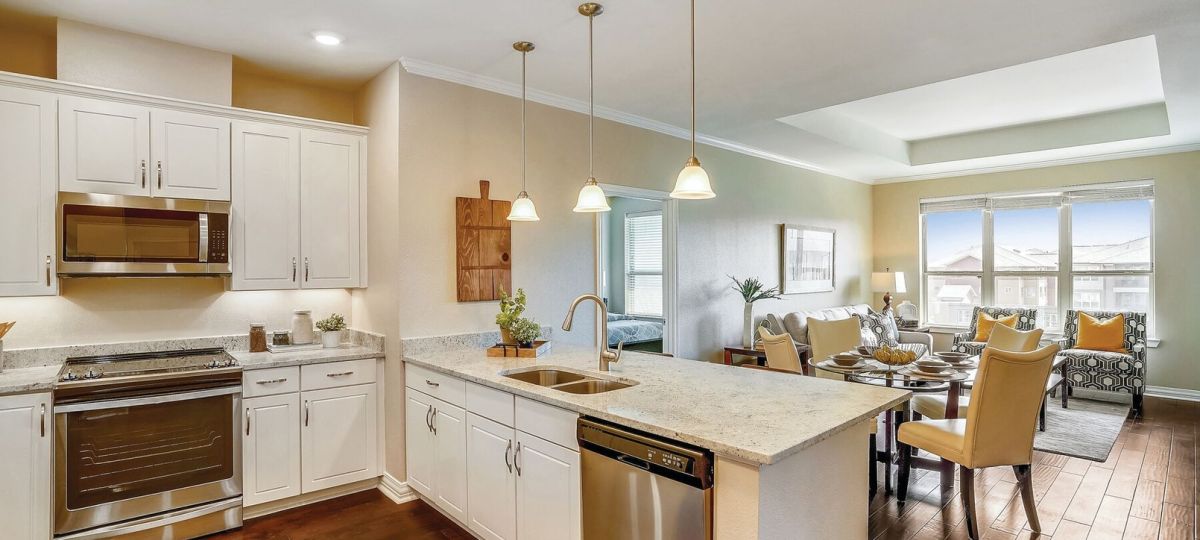 Spacious open kitchen and living area with white cabinetry, large island, wood flooring, and natural light.