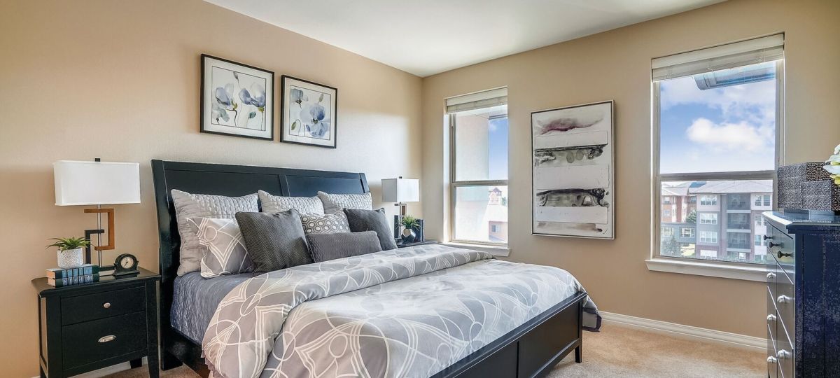 Modern bedroom with gray bedding, large windows, neutral decor, and contemporary furniture.