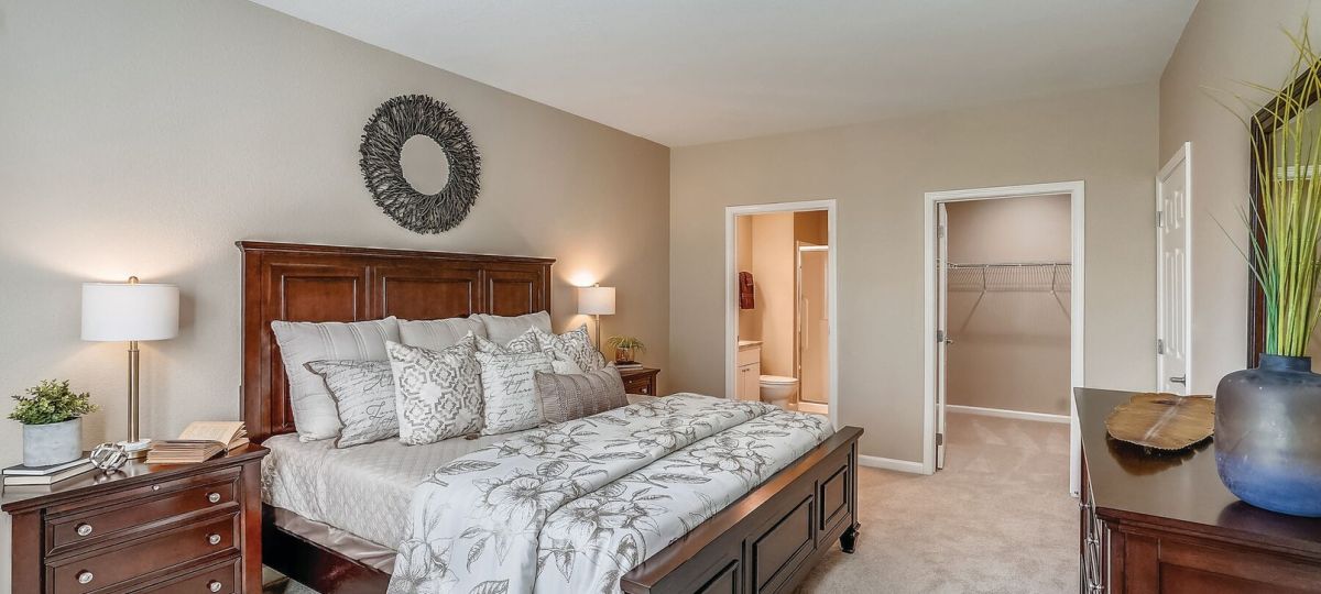 Spacious primary bedroom with wood furniture, neutral decor, plush carpeting, and walk-in closet access.