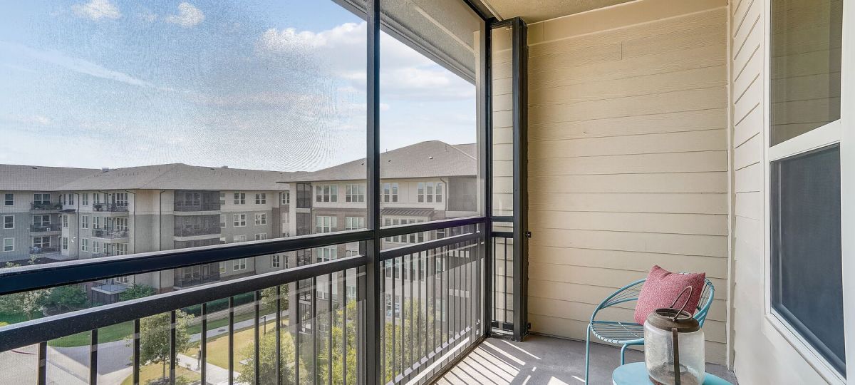 Screened-in apartment balcony with seating area, neighborhood views, and natural sunlight.