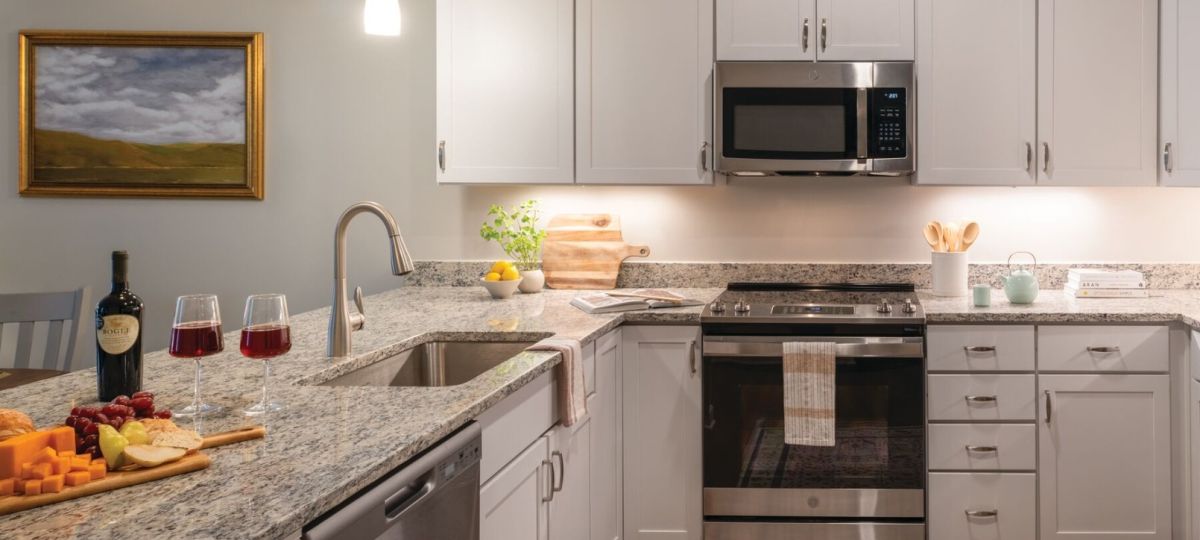 Bright modern kitchen with white cabinetry, granite countertops, stainless steel appliances, and wood flooring.