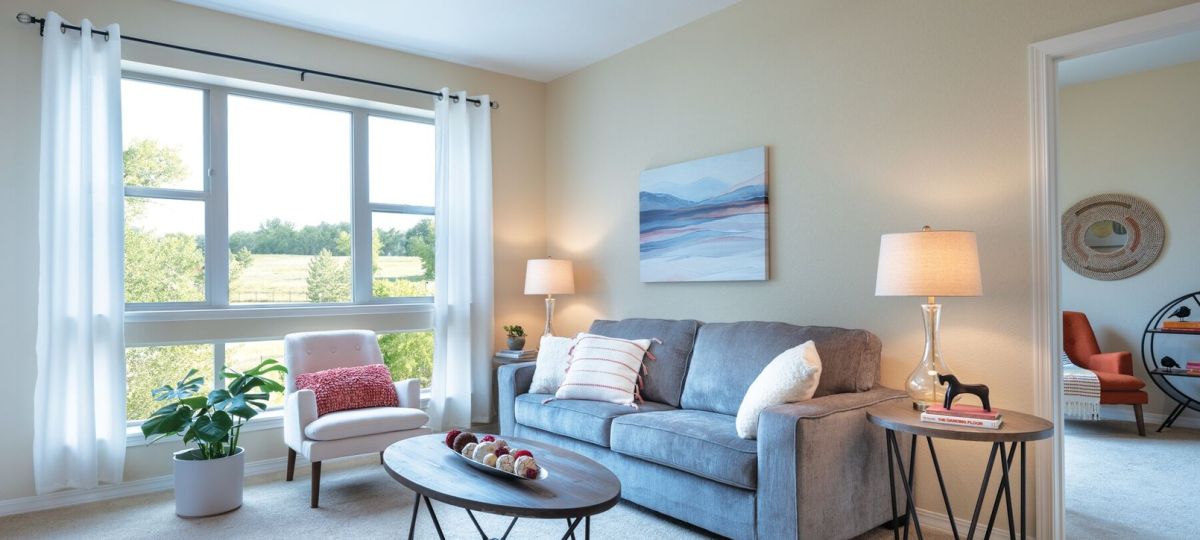 Bright and cozy living room with large picture window, soft seating, and neutral modern decor.