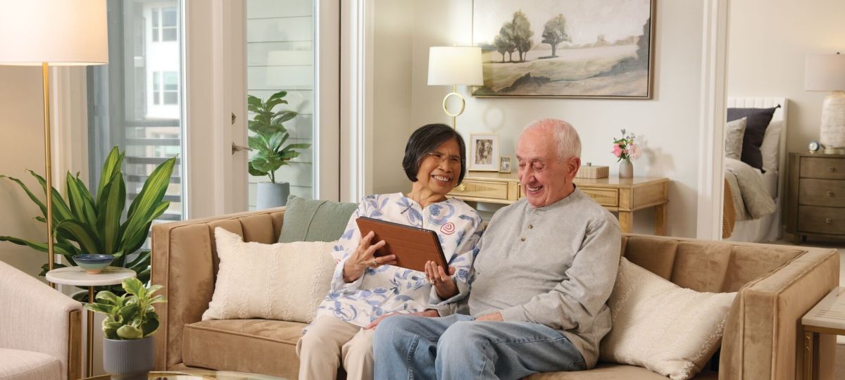a couple sitting in a living room, looking at a tablet