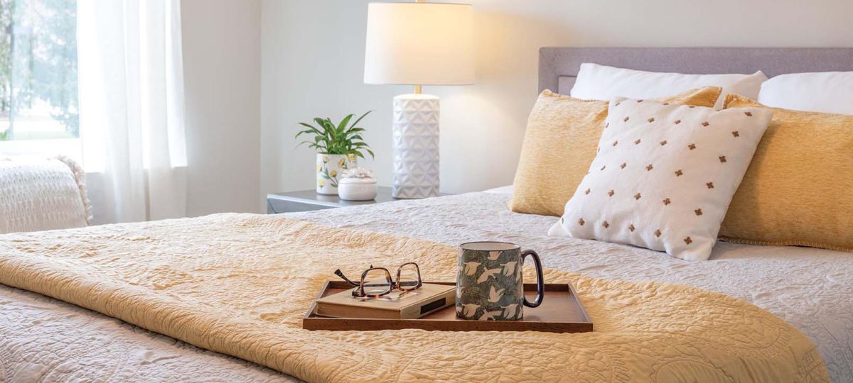 A book, glasses, and mug, on a wooden bed tray, on a bed