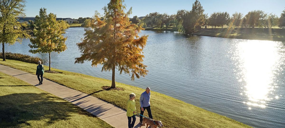 Two residents walk on a walking path next to a scenic pond