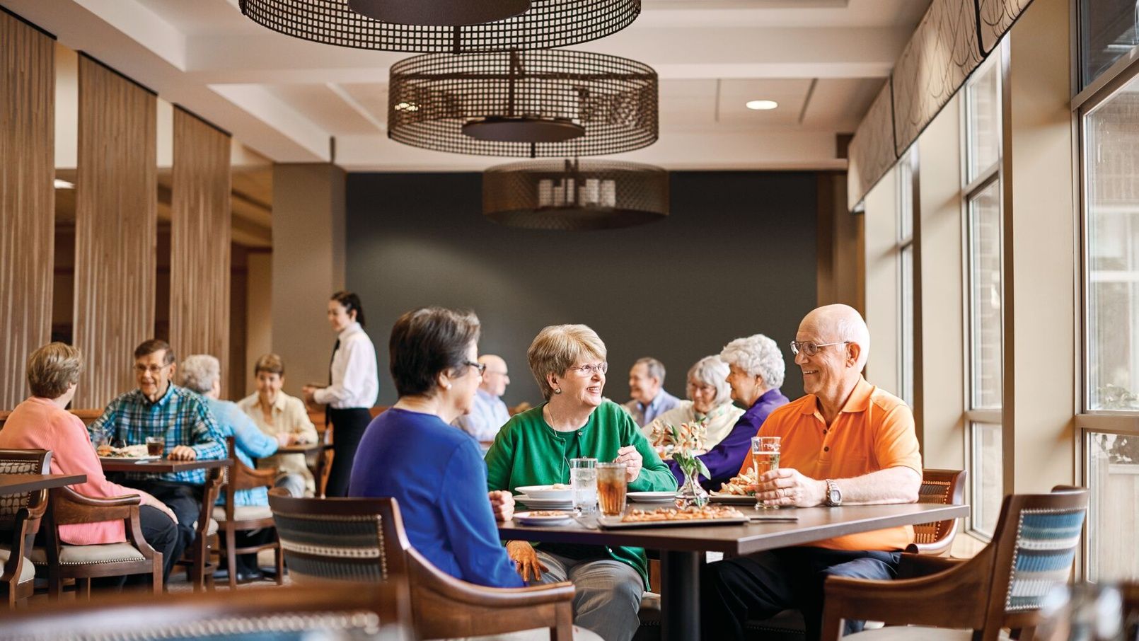 Older adults enjoying a meal together and socializing in a modern senior living dining room.