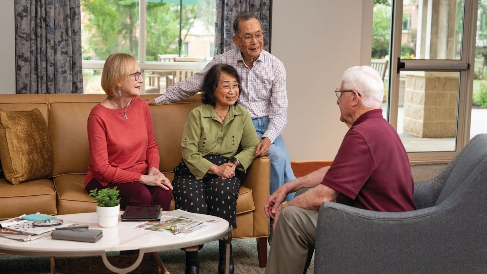 Seniors gathered in a bright community lounge, sitting and talking together in a relaxed social setting.
