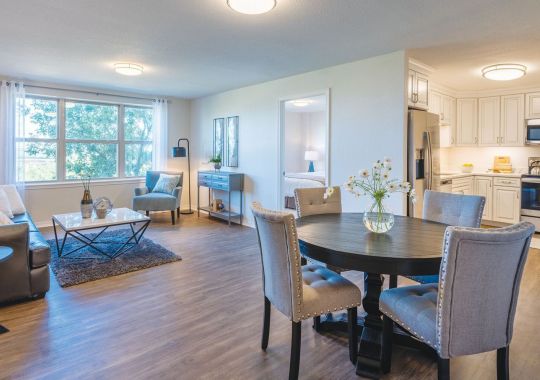 Wide shot of a bright and open living room, kitchen, and dining room in a two-bedroom apartment.